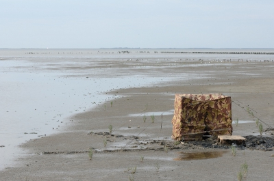 Mijn fototentje op het Wad. Ik zit op een houten bodemplank die ik in het slik heb vastgeprikt. Mijn rugzak kan ik op het pallet leggen. De vloed komt niet elke dag tot aan de tent maar als hij komt heb ik nog genoeg tijd (10 cm) om de boel op te ruimen en mij terug te trekken.